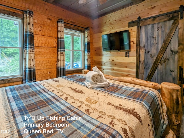 bedroom with a barn door, wooden walls, and multiple windows