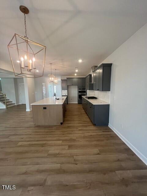 kitchen with gray cabinetry, a kitchen island with sink, sink, dark hardwood / wood-style floors, and hanging light fixtures