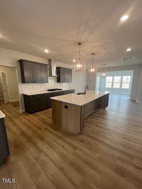 kitchen featuring tasteful backsplash, wall chimney exhaust hood, pendant lighting, a center island with sink, and dark hardwood / wood-style floors