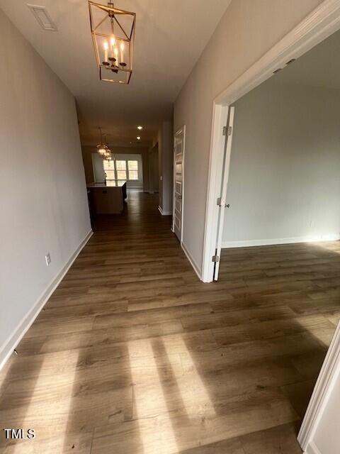 corridor with dark hardwood / wood-style floors and an inviting chandelier