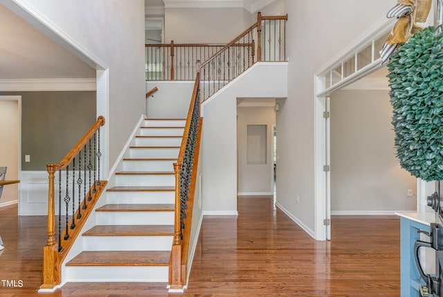 stairway featuring a high ceiling, hardwood / wood-style flooring, and crown molding