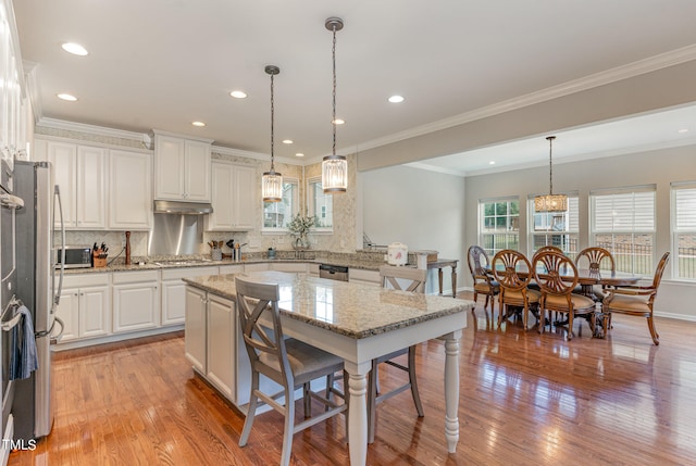 kitchen featuring backsplash, ornamental molding, light wood-type flooring, and pendant lighting