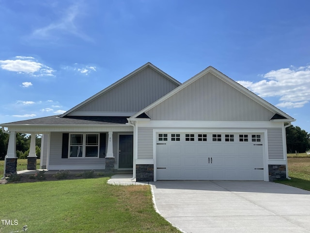 craftsman house featuring stone siding, an attached garage, a front lawn, driveway, and covered porch