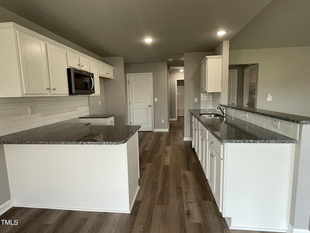kitchen featuring dark wood-style flooring, a peninsula, stainless steel microwave, dark stone counters, and a sink
