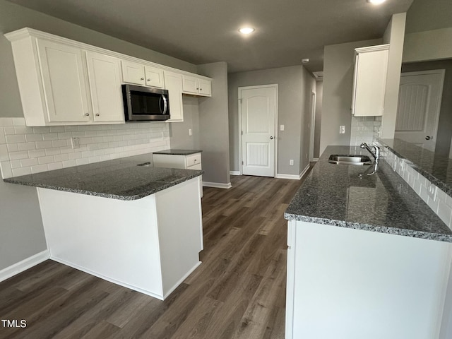 kitchen with white cabinets, a peninsula, stainless steel microwave, dark stone countertops, and a sink