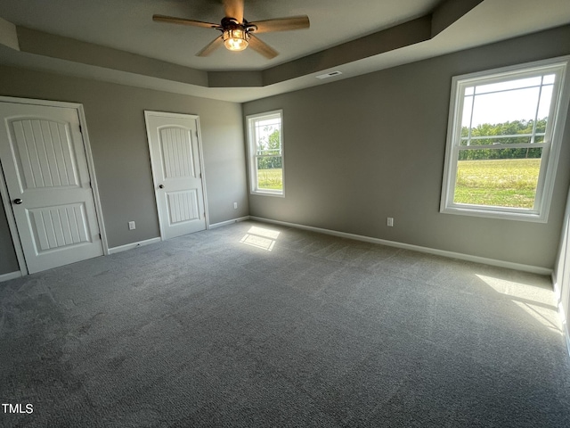 unfurnished bedroom with a tray ceiling, baseboards, visible vents, two closets, and carpet