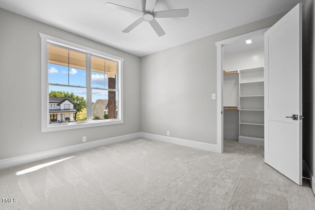 unfurnished bedroom with ceiling fan, light colored carpet, a closet, and a walk in closet