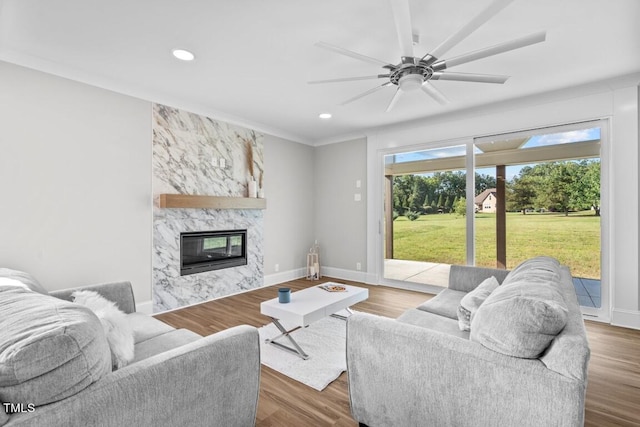 living room featuring ceiling fan, wood-type flooring, and a stone fireplace