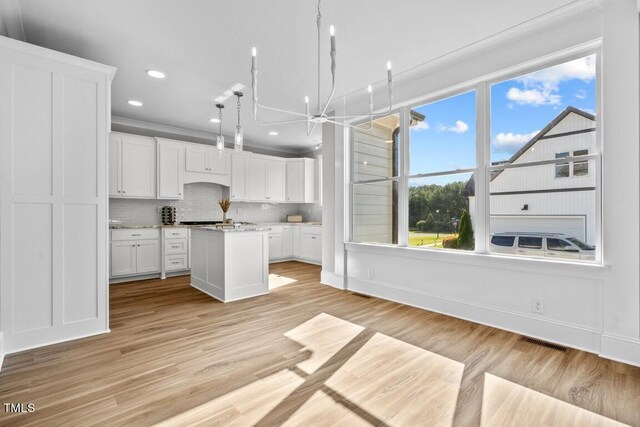 kitchen featuring white cabinetry, decorative backsplash, a kitchen island, decorative light fixtures, and light wood-type flooring