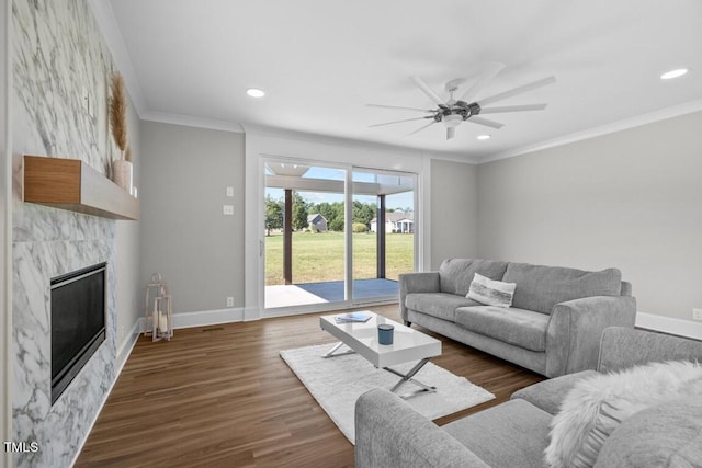 living room with a tiled fireplace, dark wood-type flooring, ornamental molding, and ceiling fan