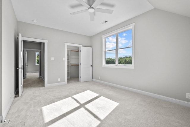 unfurnished bedroom with lofted ceiling, a walk in closet, light colored carpet, a closet, and ceiling fan