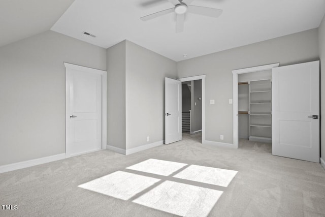 unfurnished bedroom with lofted ceiling, a spacious closet, ceiling fan, light carpet, and a closet