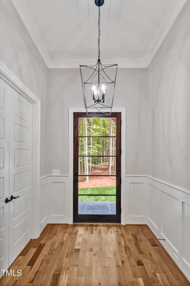 doorway to outside with light hardwood / wood-style floors, an inviting chandelier, and crown molding