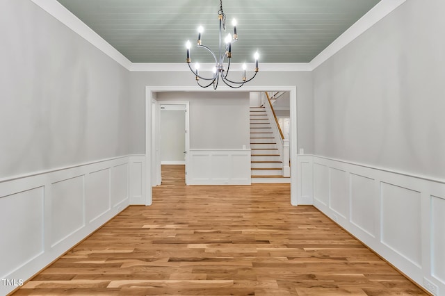 unfurnished dining area featuring light wood-type flooring, ornamental molding, and an inviting chandelier