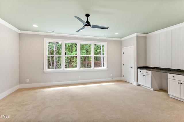 unfurnished living room with built in desk, light colored carpet, ceiling fan, and crown molding