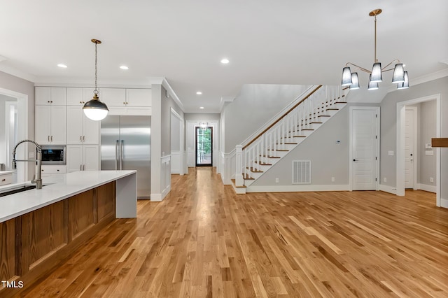 kitchen with white cabinetry, sink, built in appliances, crown molding, and decorative light fixtures