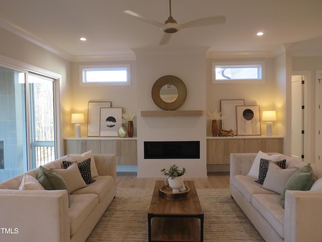 living room with ornamental molding, a large fireplace, ceiling fan, and light wood-type flooring