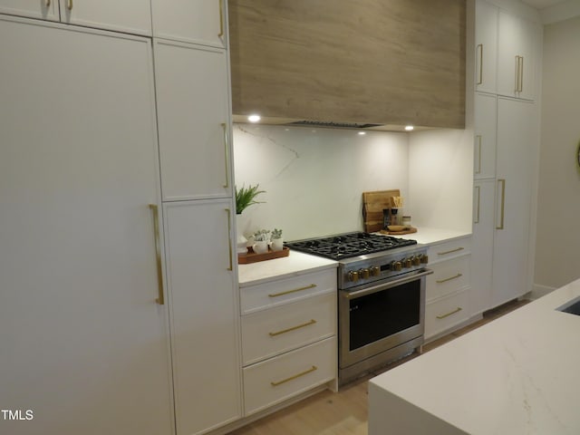 kitchen with light hardwood / wood-style flooring, stainless steel gas range oven, wall chimney exhaust hood, and white cabinets