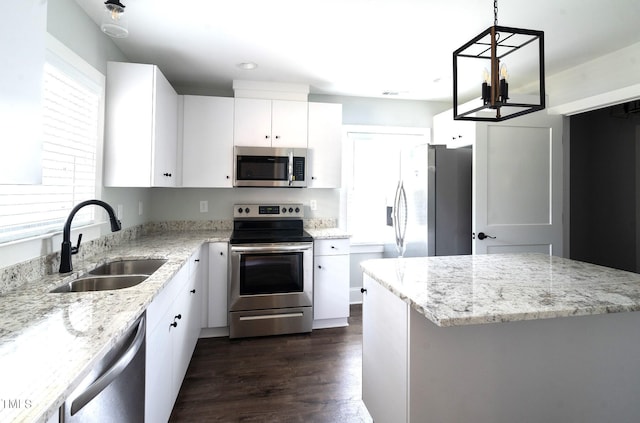 kitchen featuring sink, white cabinetry, light stone counters, appliances with stainless steel finishes, and pendant lighting