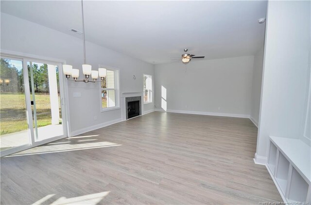 unfurnished living room featuring light wood-type flooring, ceiling fan with notable chandelier, and plenty of natural light