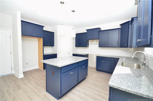 kitchen featuring sink, light stone counters, light hardwood / wood-style flooring, pendant lighting, and a kitchen island