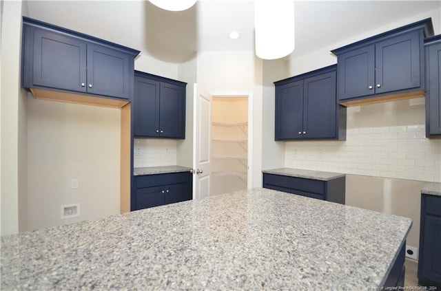 kitchen featuring light stone counters, blue cabinets, and backsplash