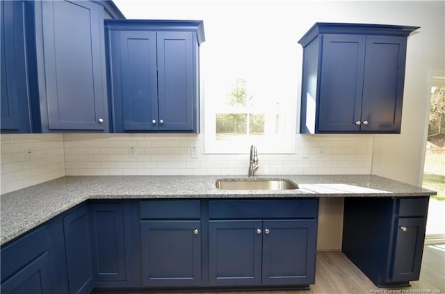 kitchen with backsplash, light stone counters, sink, blue cabinetry, and light hardwood / wood-style flooring