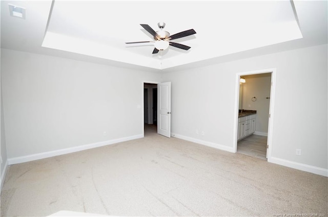 unfurnished bedroom with ceiling fan, a raised ceiling, light carpet, and ensuite bath