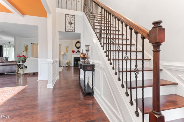 stairway with wood-type flooring, decorative columns, and a high ceiling