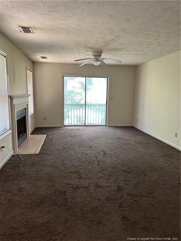 unfurnished living room featuring ceiling fan, a textured ceiling, and dark colored carpet