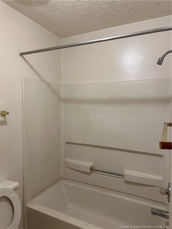 bathroom with shower / bathing tub combination, a textured ceiling, and toilet