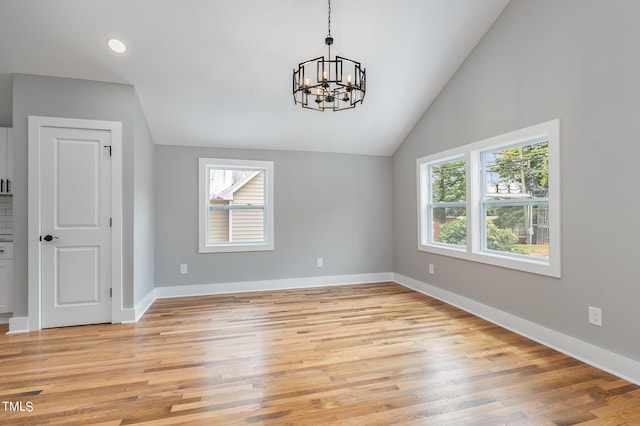 unfurnished dining area with a healthy amount of sunlight, lofted ceiling, light hardwood / wood-style flooring, and a notable chandelier