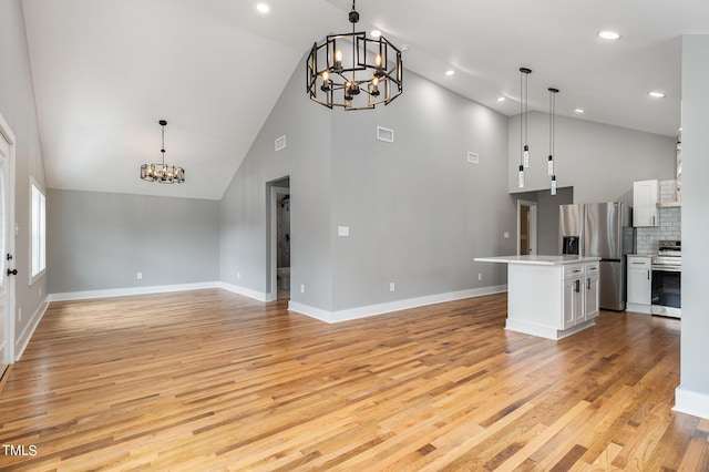 unfurnished living room featuring a notable chandelier, vaulted ceiling, and light wood-type flooring