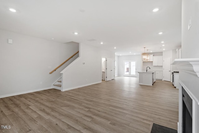 unfurnished living room with an inviting chandelier, sink, and light hardwood / wood-style floors