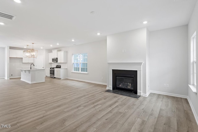 unfurnished living room featuring sink, a notable chandelier, and light hardwood / wood-style flooring