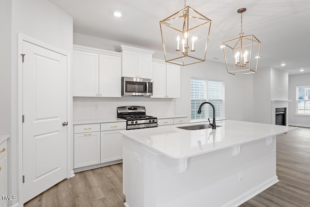 kitchen with sink, hanging light fixtures, stainless steel appliances, white cabinets, and a center island with sink