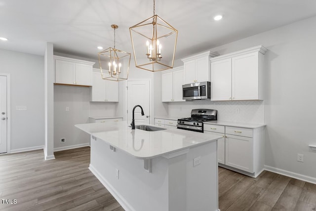 kitchen with appliances with stainless steel finishes, white cabinetry, sink, hanging light fixtures, and a center island with sink