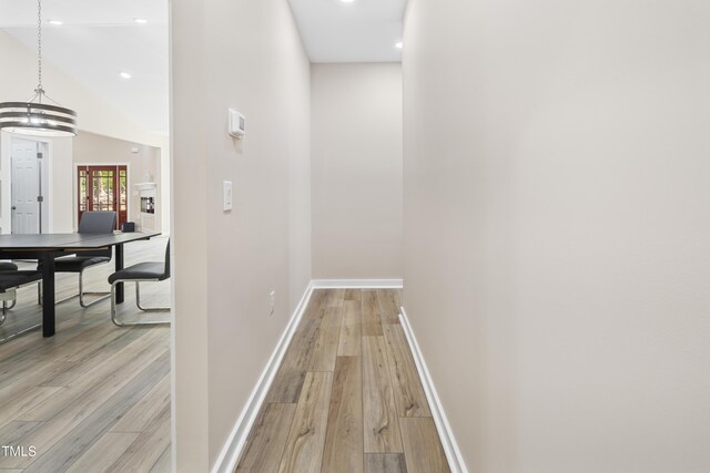 corridor with high vaulted ceiling, light hardwood / wood-style flooring, and a chandelier