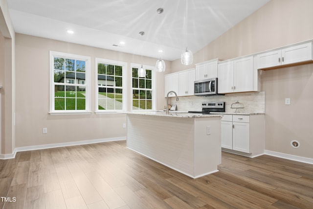 kitchen featuring white cabinetry, light stone counters, stainless steel appliances, wood-type flooring, and a center island with sink