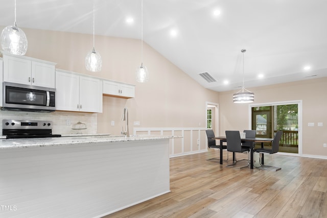 kitchen featuring white cabinetry, light stone counters, pendant lighting, stainless steel appliances, and light hardwood / wood-style flooring