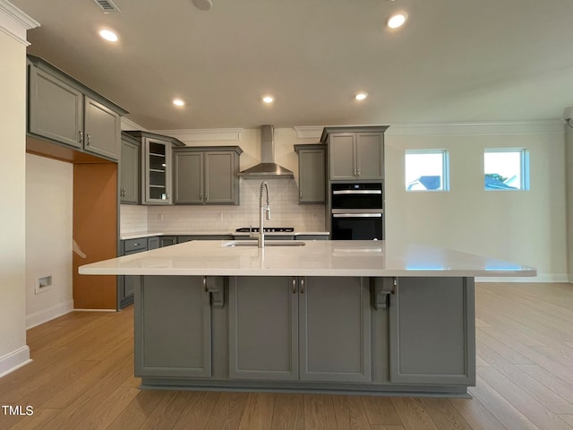 kitchen featuring a large island with sink, wall chimney exhaust hood, and gray cabinets