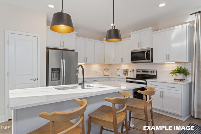 kitchen with an island with sink, hanging light fixtures, white cabinets, and stainless steel appliances