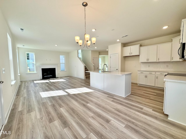 kitchen featuring pendant lighting, backsplash, a kitchen island with sink, white cabinets, and sink