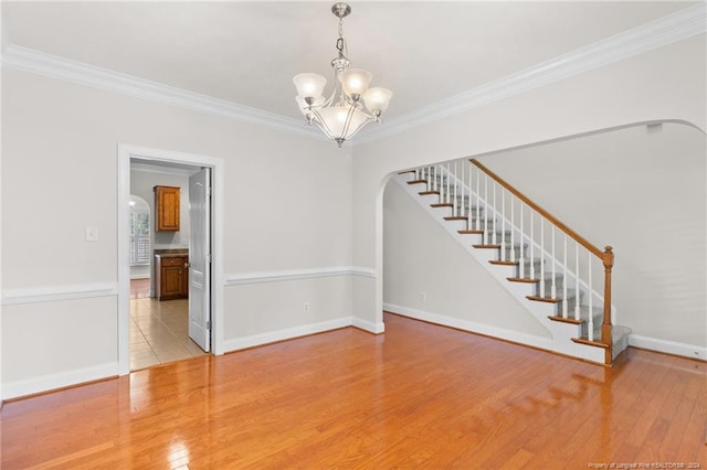 empty room with light wood-type flooring, ornamental molding, and a chandelier