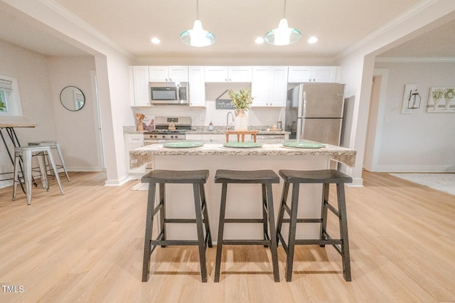 kitchen with appliances with stainless steel finishes, white cabinets, hanging light fixtures, a center island, and crown molding