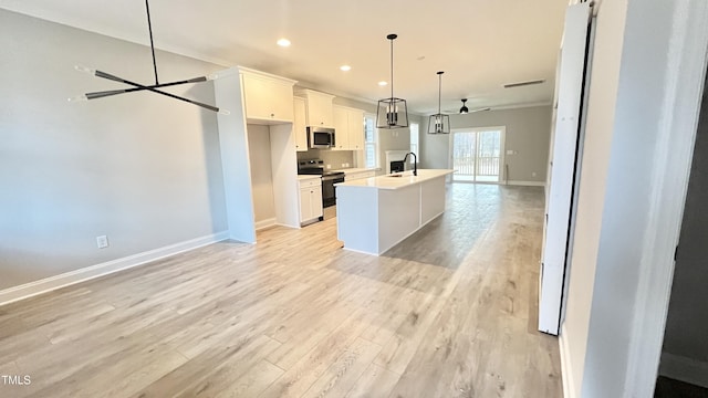 kitchen featuring stainless steel appliances, light hardwood / wood-style flooring, decorative light fixtures, a center island with sink, and white cabinets