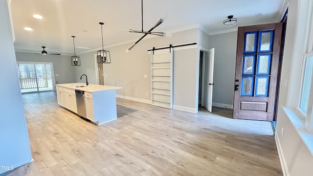 kitchen featuring dishwasher, sink, a barn door, pendant lighting, and a center island with sink