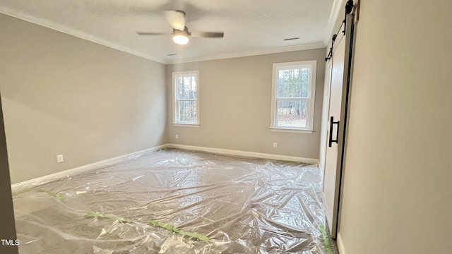 spare room featuring ceiling fan, a healthy amount of sunlight, a barn door, and crown molding