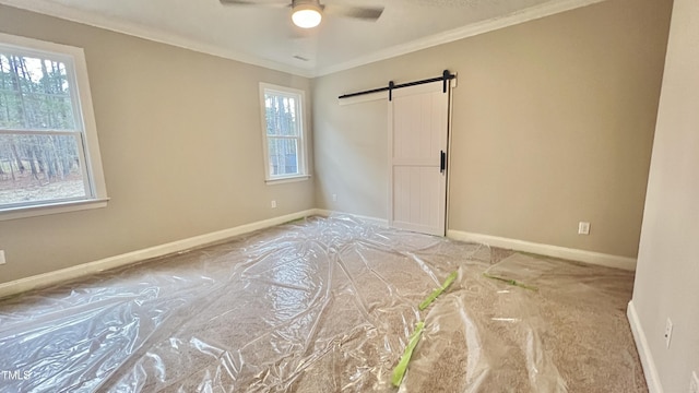 spare room featuring a barn door, ceiling fan, and crown molding