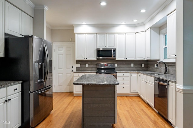 kitchen with appliances with stainless steel finishes, white cabinetry, sink, a kitchen island, and dark stone countertops